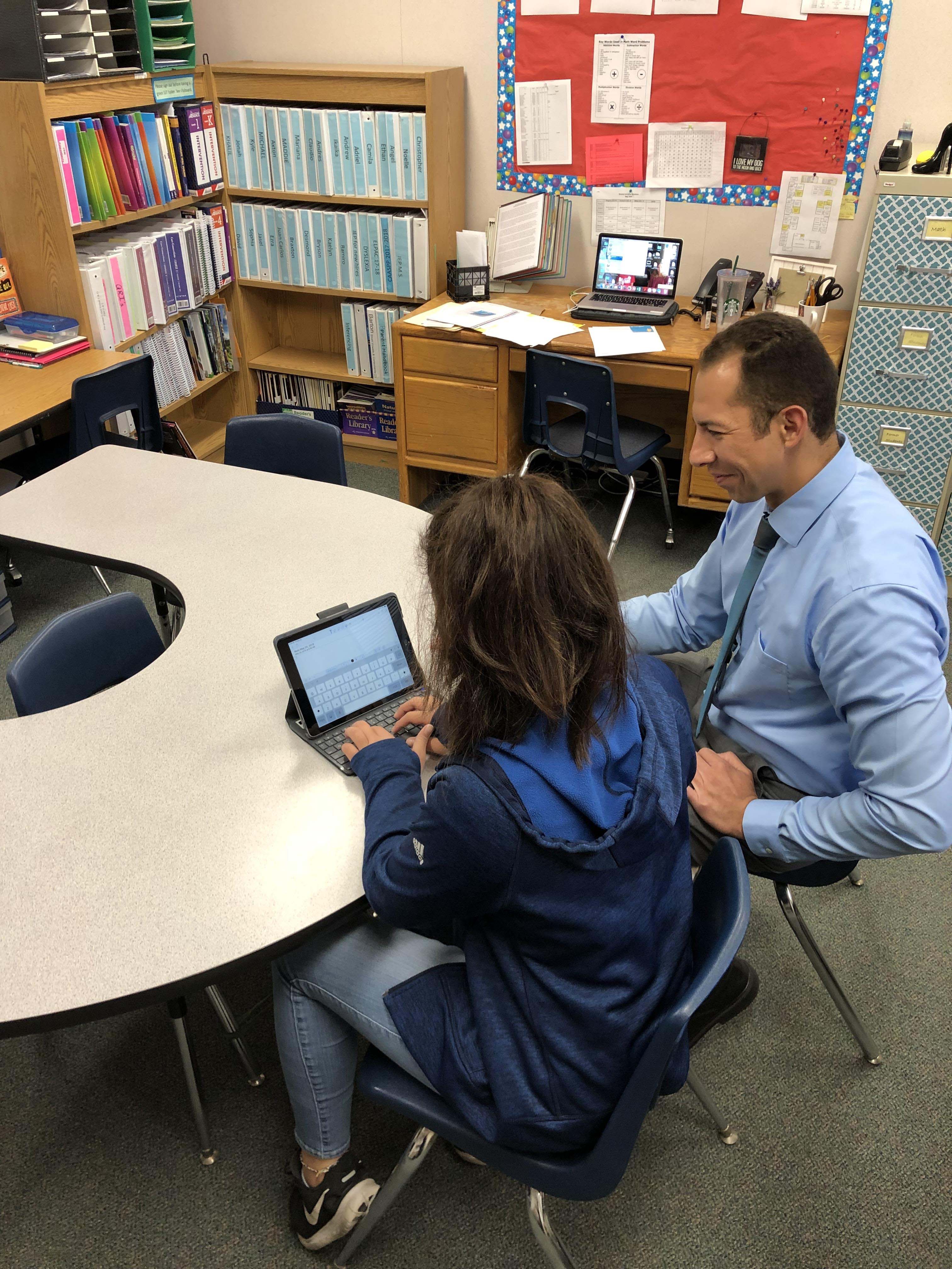 Jerry working with a student in the classroom on a device. 